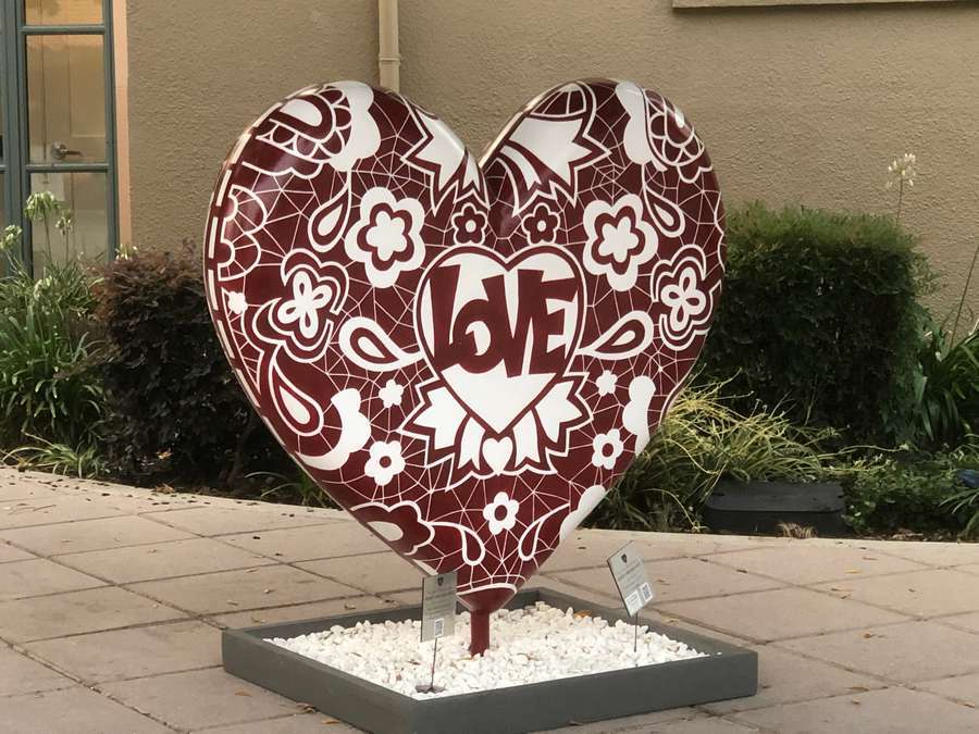 Burgundy and white decorative heart sculpture with "LOVE" text and floral patterns in outdoor plaza setting