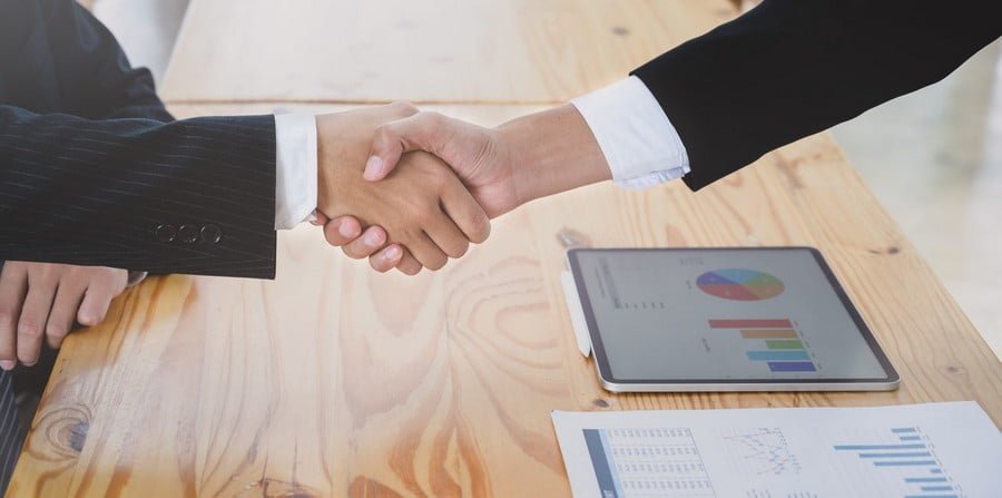 Business professionals shaking hands over a wooden desk with marketing analytics charts and data reports visible