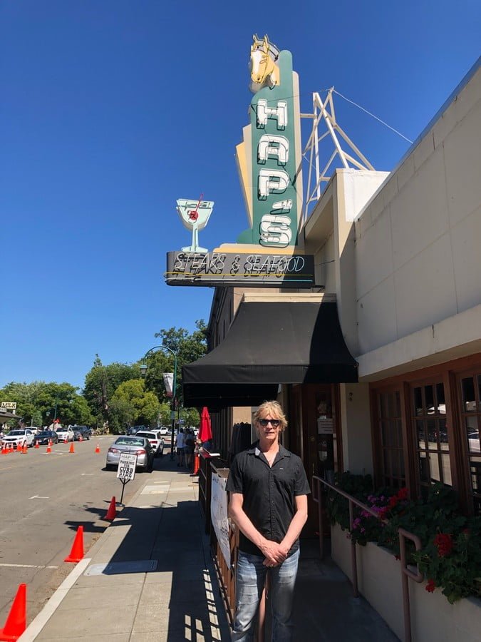 Man standing under vintage neon Haps restaurant sign in Pleasanton