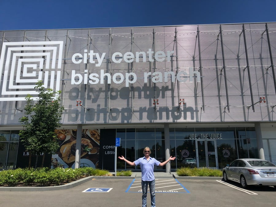 Man with arms raised in front of City Center Bishop Ranch shopping mall in San Ramon, California