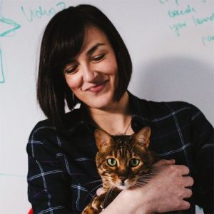 Woman holding tabby cat in front of whiteboard with marketing notes