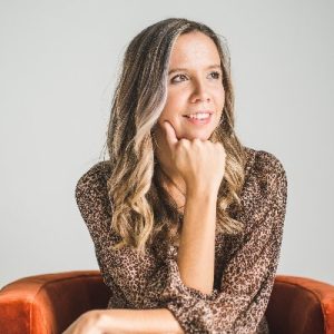 Julia McCoy in a brown patterned blouse sitting on an orange chair