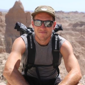 Man wearing cap and sunglasses with hiking backpack in desert landscape