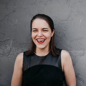 Melanie Deziel smiling in front of textured gray wall wearing black sleeveless top