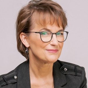 Professional headshot of woman with brown hair, glasses, and black jacket