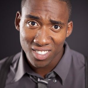 Professional headshot of man in gray button-up shirt against dark background