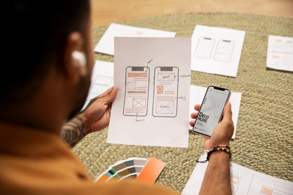 Designer reviewing mobile app wireframes and prototype on smartphone during web design planning session