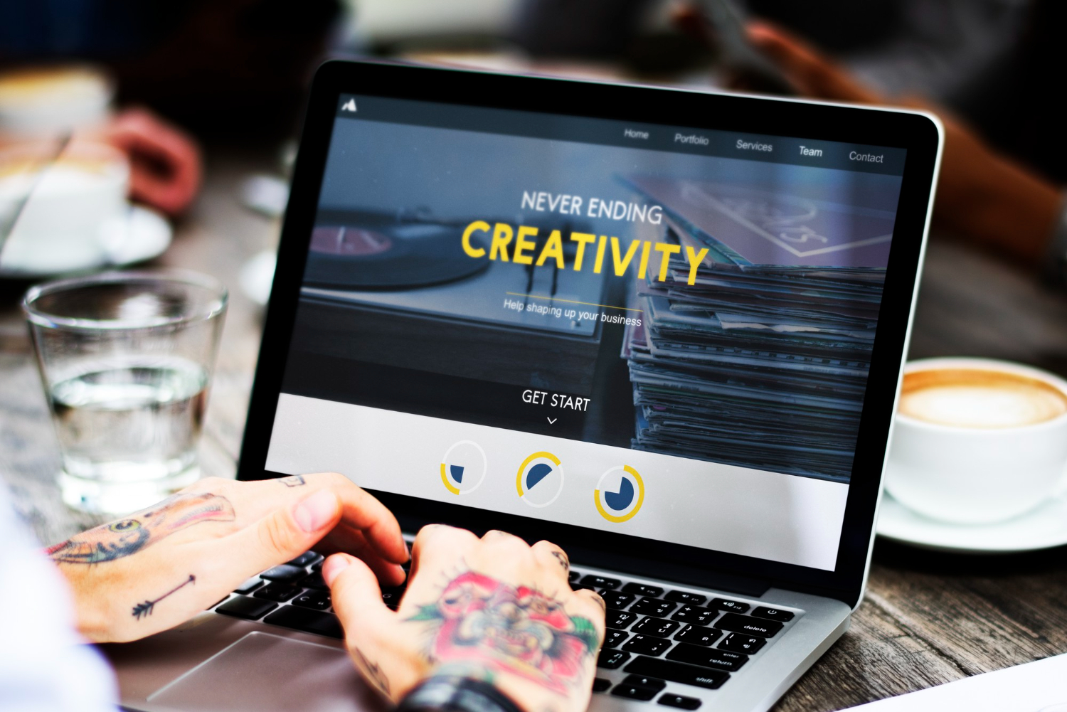 Woman with tattooed hands using laptop displaying digital marketing website with "Never Ending Creativity" tagline