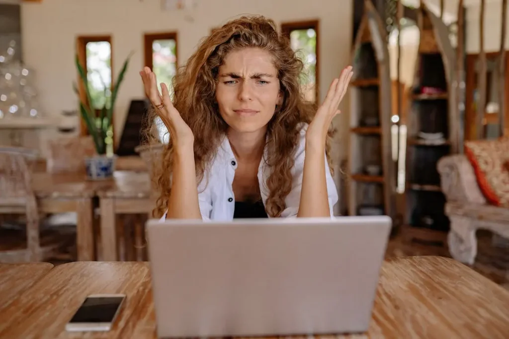 Frustrated woman with hands raised at laptop, expressing confusion or frustration with digital marketing campaign
