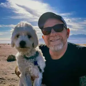 Man with white dog on beach, mountains in background