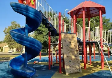 Colorful playground equipment with blue spiral slide and red climbing tower on safety surfacing