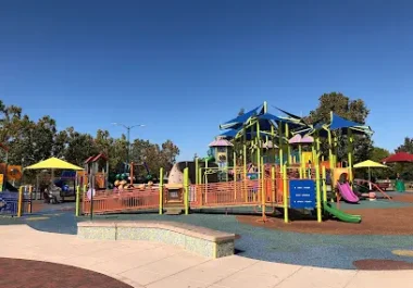 Heather Farm Park playground with yellow and blue equipment on mulch surface under clear sky