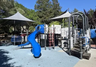 Community playground with blue slide, climbing structures, and shade tents in Santa Rosa