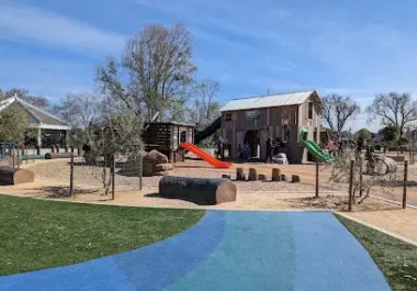 Kennedy Park playground with blue walking path, wooden structures, and play equipment