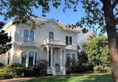 Historic white Victorian house with green lawn and large tree in Mountain View