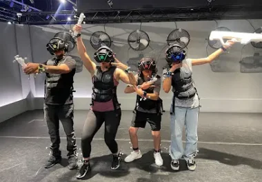 Group of four people wearing VR headsets with arms raised in excitement inside an indoor VR gaming arena