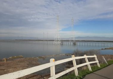White fence overlooking bay with bridge and transmission towers