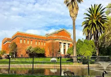 Historic red brick building with white columns behind black iron fence, palm trees, Stockton