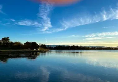 Tranquil shoreline landscape with blue sky, trees, and calm water reflection